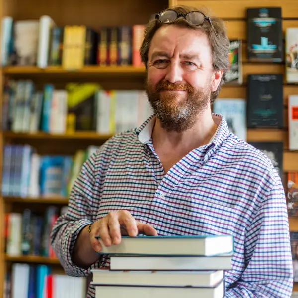 Uomo, un libraio con camicia a scacchi, regge alcuni libri nella sua libreria