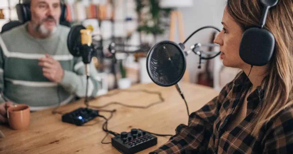 Una postazione per podcasting con microfono, cuffie e computer su una scrivania di legno.