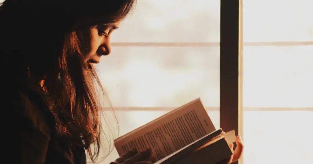 donna legge libro nella luce del sole che tramonta seduta vicino ad una finestra