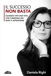 Copertina del libro "Il successo non basta" di Daniela Righi, edito da Poliedricamente Edizioni. L'immagine in bianco e nero mostra un primo piano intenso dell'autrice, una donna con occhiali e capelli scuri che guarda frontalmente l'obiettivo con una mano sotto il mento. In alto a sinistra, il titolo spicca con la parola "NON BASTA" in rosso, seguito dal sottotitolo: "Quando vivi una vita che funziona ma non ti appartiene". In basso a sinistra è presente il logo della casa editrice.