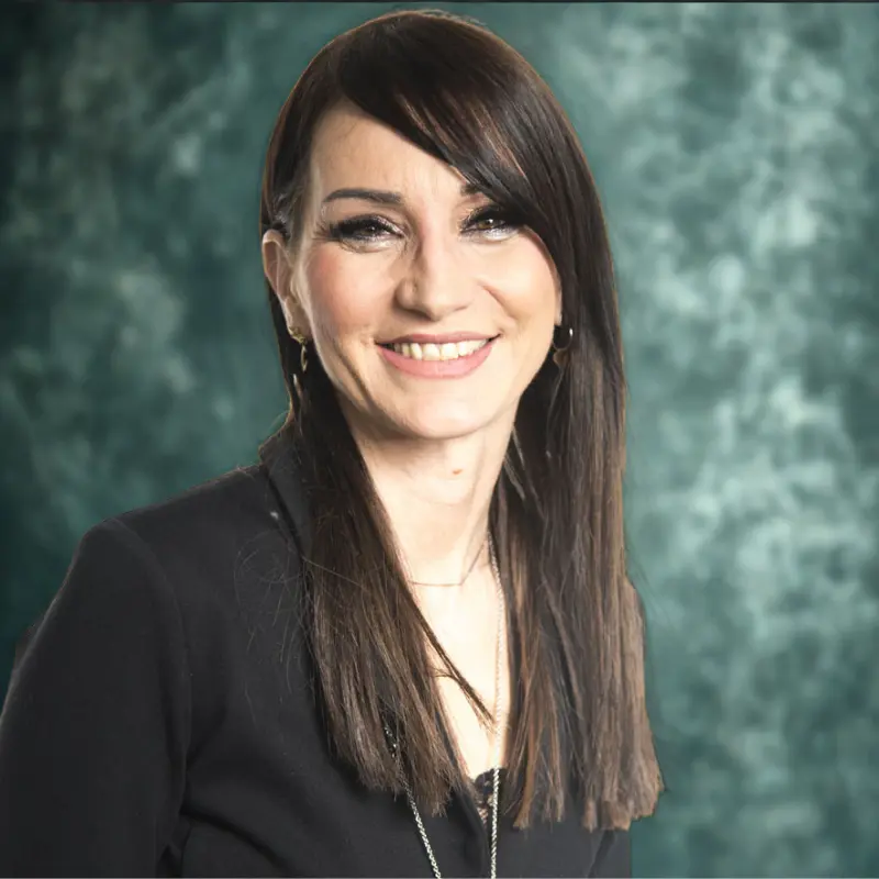 Gloria Chiarini autrice e coach, immagine scattata in uno studio fotografico mezzobusto, sfondo verde acqua scuro