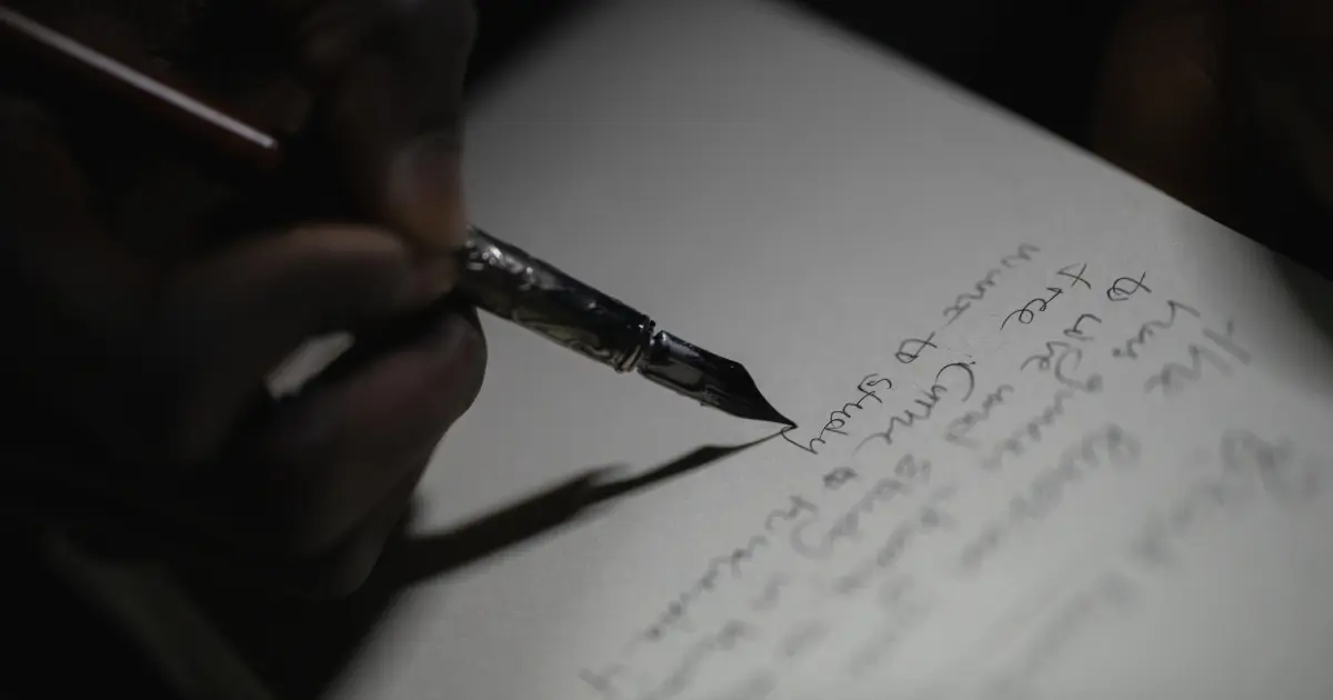 Una persona scrive una proposta editoriale su un taccuino con una penna stilografica.